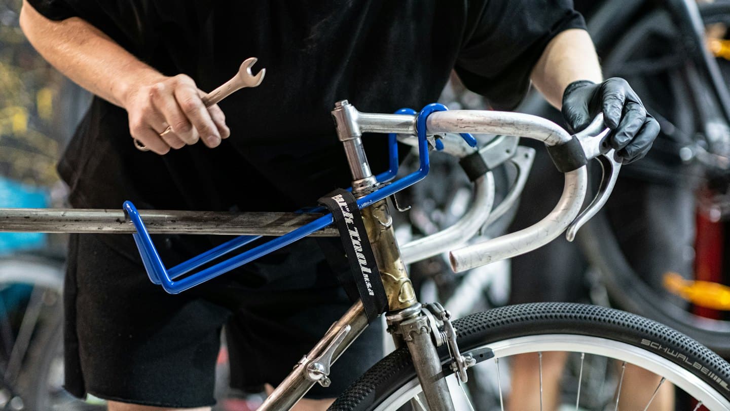 Bike mechanic works on bicycle handlebars with a wrench.