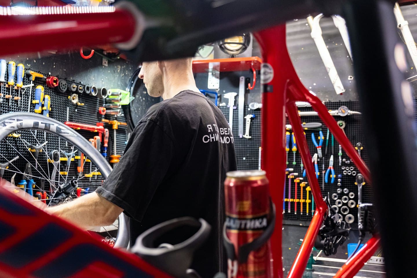Man repairs a bicycle wheel in a tool-filled shop.