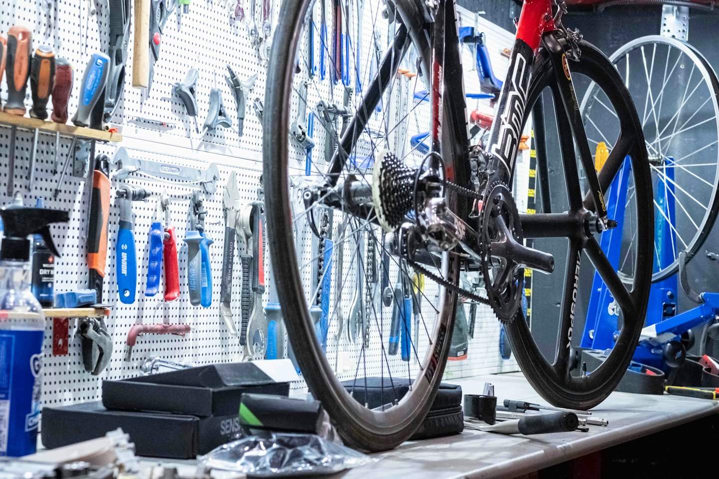 Road bike hangs above workbench in a tool-filled repair shop.