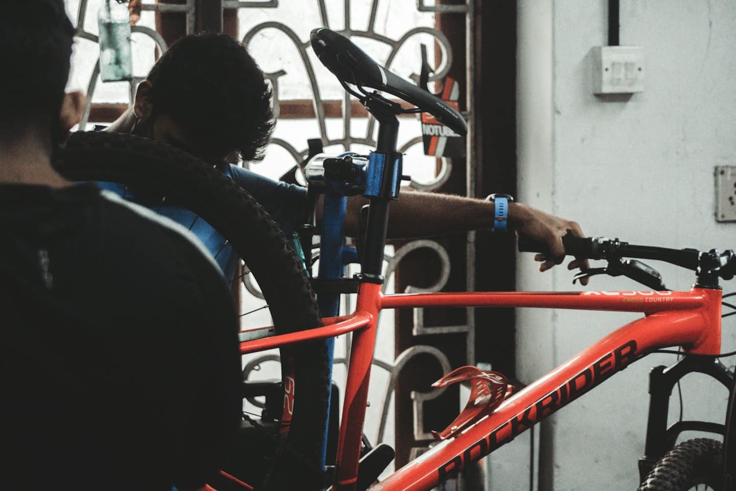Mechanic repairs an orange mountain bike on a blue stand.